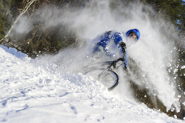 Extreme cyclist riding bicycle near snowbanks of mountain slope, winter sport, cross country biking near forest in cool sunny day