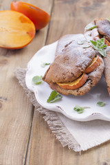 Homemade pastries with fresh persimmons, for breakfast, white plate on a napkin. Wooden table. Free space for text or advertising.