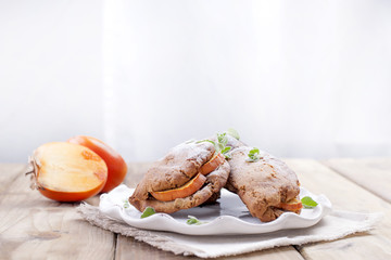 Homemade pastries with fresh persimmons, for breakfast, white plate on a napkin. Wooden table. Free space for text or advertising.