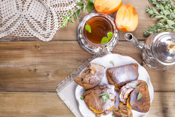 Homemade pastries with persimmons, for breakfast. Beautiful glass with tea. Kettle. A wooden table, a place for text or advertising. View from the top.