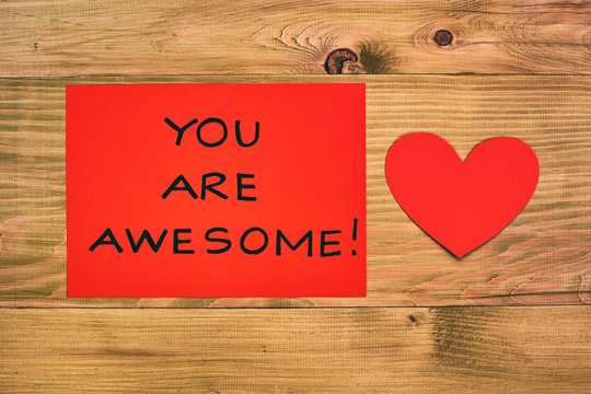 Message you are awesome and heart shapes on red paper on wooden table.