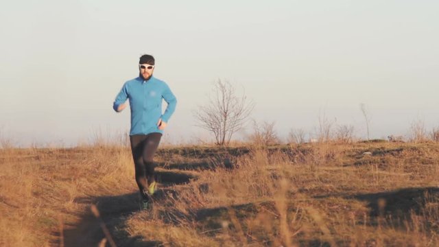 young man trail runner training outdoors in the fields, sunset in lake background 