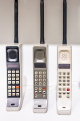 Three large vertical vintage old portable outdated cellphones phones standing on display with...