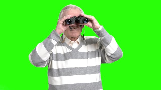 Senior man using binoculars. Grantfather looking into binoculars and looking for something, green hroma background.