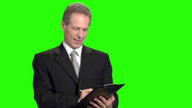 Smiling mature man writing down on clipboard. Man doing remark on green hromakey background.