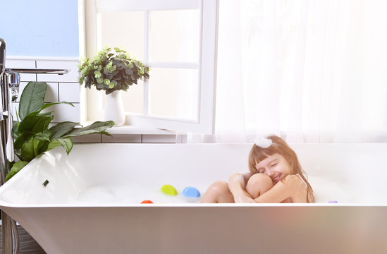  Happy little baby girl sitting in bath tub  in the bathroom