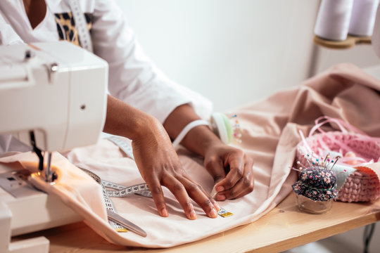 african seamstress working with pink fabric takes measures