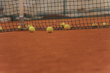 Tennis balls on red court with gray net