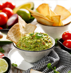 Guacamole is a traditional Mexican dip made of avocado, onion, tomatoes, coriander, chilli peppers, lime and salt with the addition of tortilla in a ceramic bowl.  Healthy vegetarian dish 