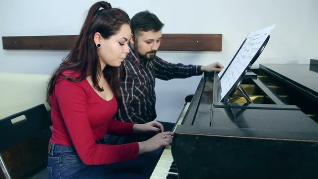 Male teacher with young girl student playing piano in musical school
