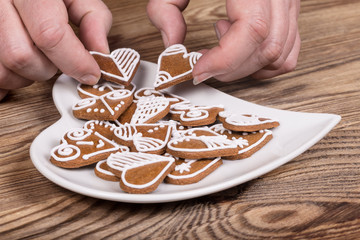 Female hands and preparation of sweet ornate gingerbreads for good luck. Valentine's cookies and plate in heart shape on a wood table. Idea of cooking, holidays and celebrations.
