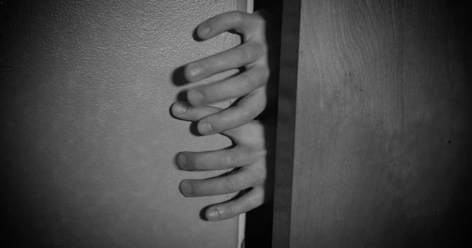 Scary zombie-like fingers try to enter a room from behind a closed door. Old film look stylized treatment.	