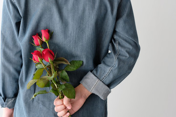 Valentine concept, Man holding red roses hiding on back on white background