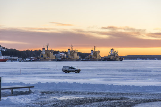 En bil k&ouml;r p&aring; isen utanf&ouml;r S&ouml;dra Hamnen i Lule&aring; med isbrytanra vid LKAB hamnen i bakgrunden