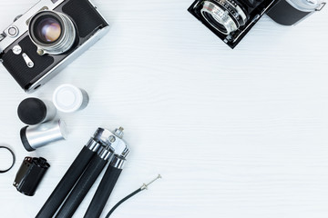 old classic photo cameras, roll films, and tripod on white wooden background flat view