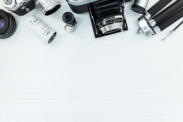vintage photo cameras, negative films, lens and tripod on white table background with copy space