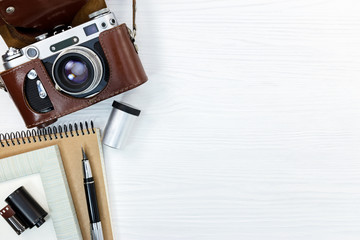 old retro camera in leather cover, notebook, pen, and roll film on white background flat view