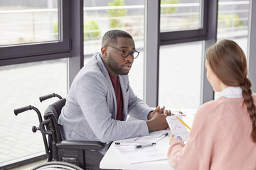 Disabled male boss has dark skin, dressed in formal cothes, analyzes budget receipts and outlays...