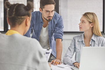 Fototapeta premium Indoor shot of diverse group communicate with each other in office, creat new marketing innovative project, work on laptop and do paper work, share opinions during conference. Team work concept