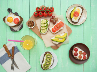 Sandwich with ovaries, with avocado, with tomato and cucumber, with kiwi, grapes and glass of lemonade on the table.
