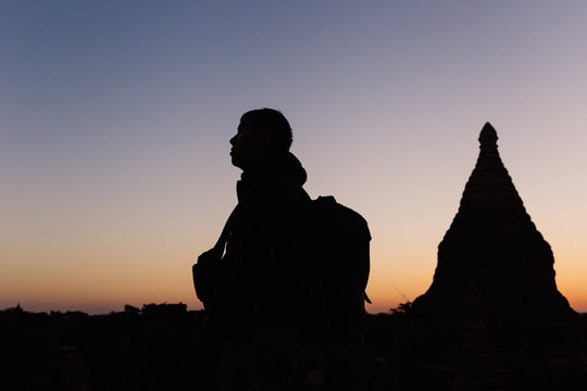 Silhouette of young travel man watching sunrise in temple pagoda area.