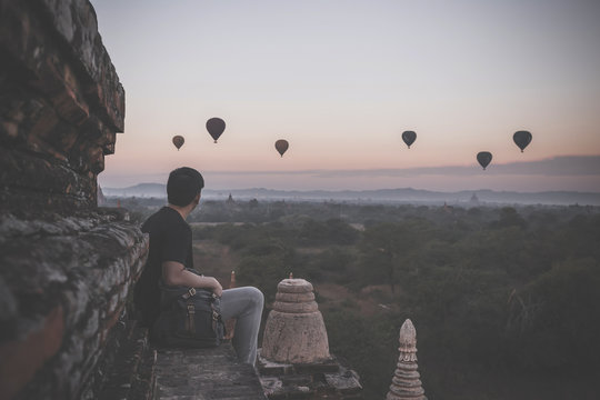 Silhouette of young male backpacker sitting and watching hot air balloon travel destinations in Bagan, Myanmar.