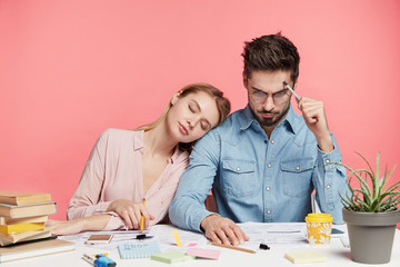 Photo of exhausted sleepy female tired after hard work on course or diploma paper, work with scientific literature. Focused brunet handsome man studies document, tries understand information