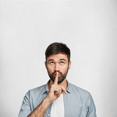 Vertical shot of secret handsome male student asks to keep silence during exam, keeps fore finger...
