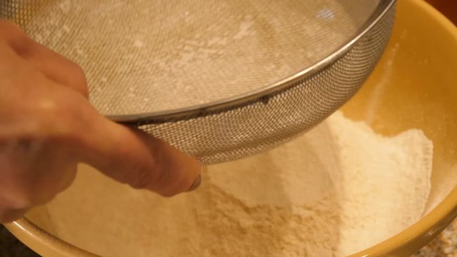 Womans hand civing flour into her mixing bowl