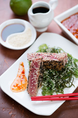 Fototapeta na wymiar Fried tuna steak on a bed of seaweed salad with sesame seeds and sauce, closeup, selective focus