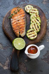 Rustic wooden serving board with roasted salmon fillet, zucchini and dipping sauce, studio shot