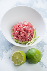 White bowl with tuna fillet tartare on a bed of guacamole, white concrete background, vertical shot