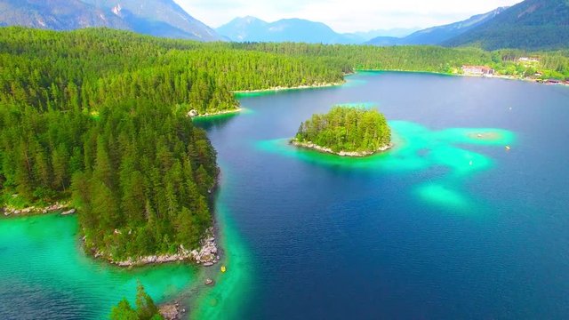 Green islands in mountain lake Eibsee beneath Zugspitze peak. Drone flight over a Germany's most beautiful glacier lake with clear emerald green water in Bavaria Alps. Germany, Central Europe. 
