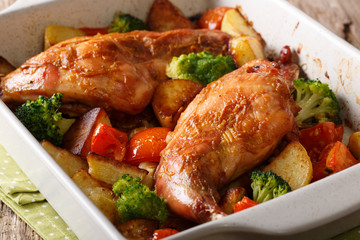 Delicious baked rabbit legs with potatoes, broccoli and tomatoes close-up in a baking dish on a table. horizontal