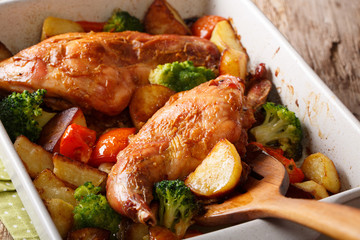 rabbit baked with potatoes, broccoli and tomatoes close-up in a baking dish on a table. horizontal