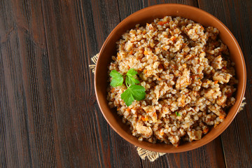 Boiled buckwheat in a bowl with pieces of chicken meat and cilantro on a brown wooden table.