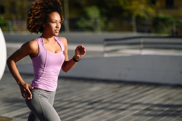 Black woman, afro hairstyle, running outdoors in urban road.