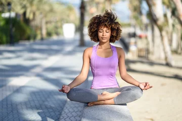 Tuinposter Black woman, afro hairstyle, in lotus asana with eyes closed in the beach © javiindy