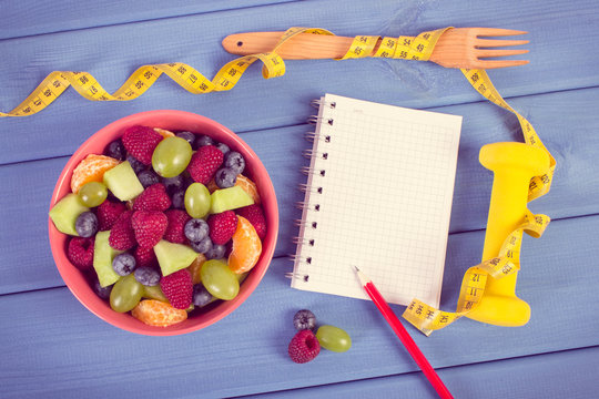 Fruit salad, tape measure with dumbbells and notepad for writing notes, healthy lifestyle and nutrition concept