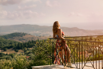 Beautiful female in a summer dress on a balcony in the background of Greek landscapes