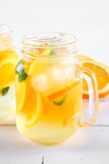 Orange detox water in mason jars on a white wooden table. Healthy food, drinks.