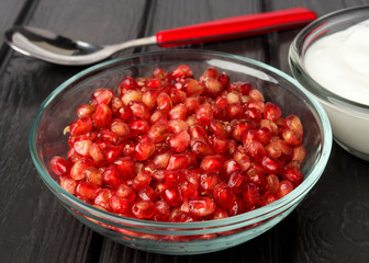 group of pomegranate grains in glass bowl on black wood