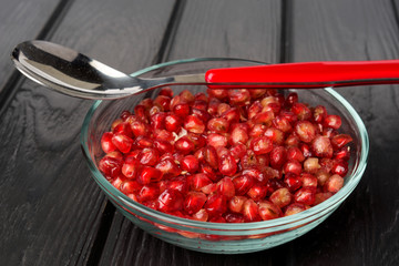 group of pomegranate grains in glass bowl on black wood