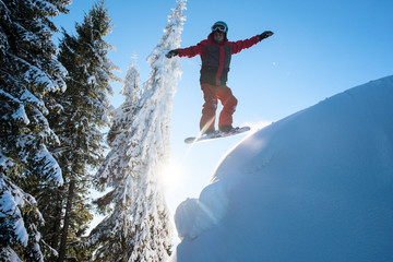 Freerider snowboarder jumping in the air while riding on the slope in the mountains. Blue sky and...