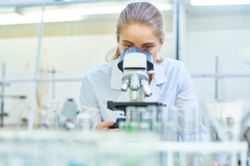 Portrait of young female scientist looking in microscope while working on medical research in science laboratory, copy space - obrazy, fototapety, plakaty