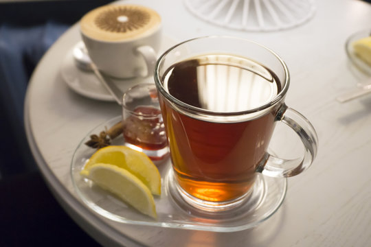A transparent glass mug of black tea and a lemon close-up on a white round table in a cafe.