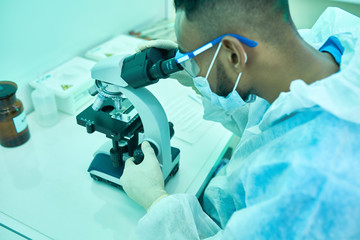 High angle portrait of young Middle-eastern scientist using microscope while working in laboratory doing medical research