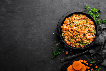 Carrot braised with fresh green peas in creamy milk sauce in stewpan, vegetable saute on black background, top view