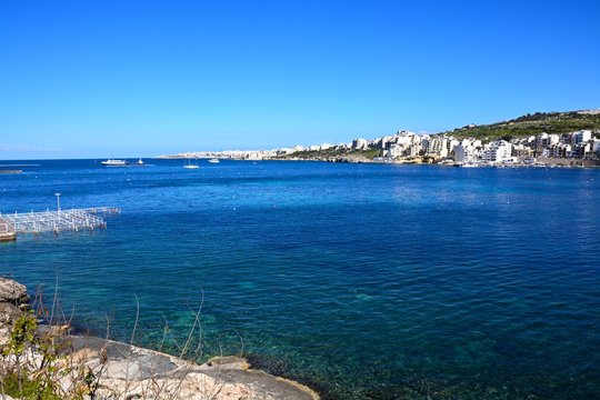 Rocky shoreline with views across the sea towards St Pauls Bay, San Pawl, Malta.