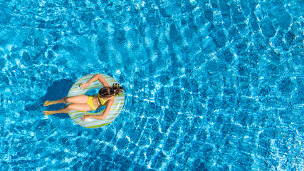 Aerial top view of girl in swimming pool from above, kid swims on inflatable ring donut , child has fun in water on family vacation
